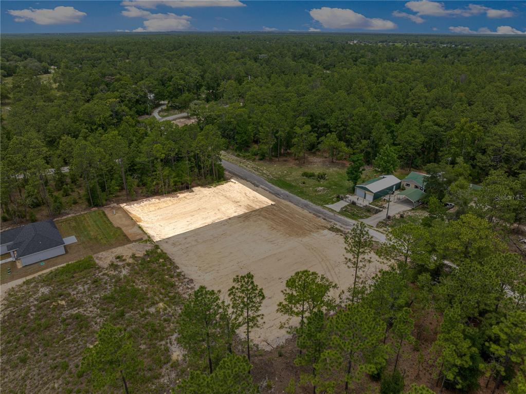 An aerial view shows a cleared, sandy residential lot surrounded by trees and nearby houses — SW 38TH PLACE, OCALA, FL