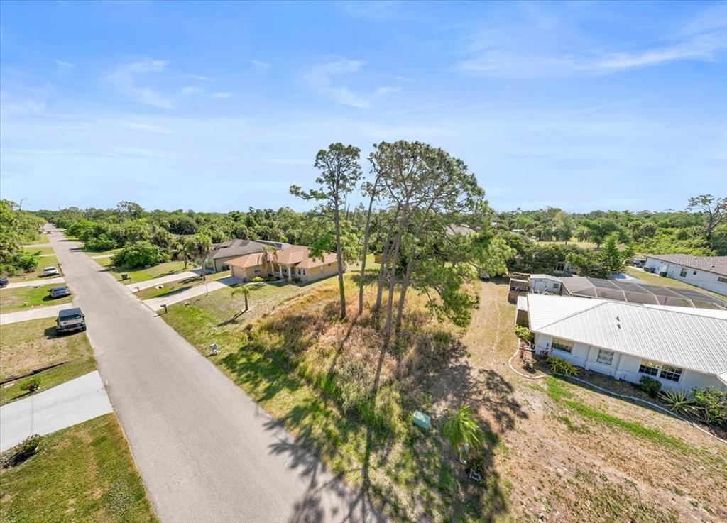 An aerial view shows a vacant, tree-covered residential lot situated between two houses and a road — SABRINA TERRACE, NORTH PORT, FL