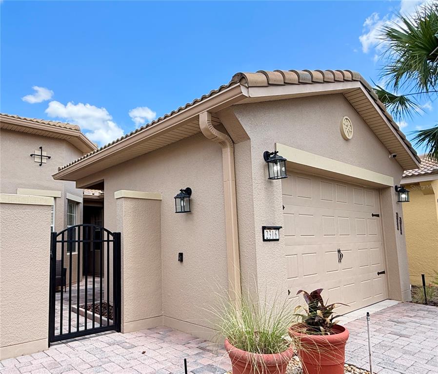 The exterior of a tan stucco house features a garage, a gated courtyard, and pavers — 2316 PALM TREE DRIVE, KISSIMMEE, FL