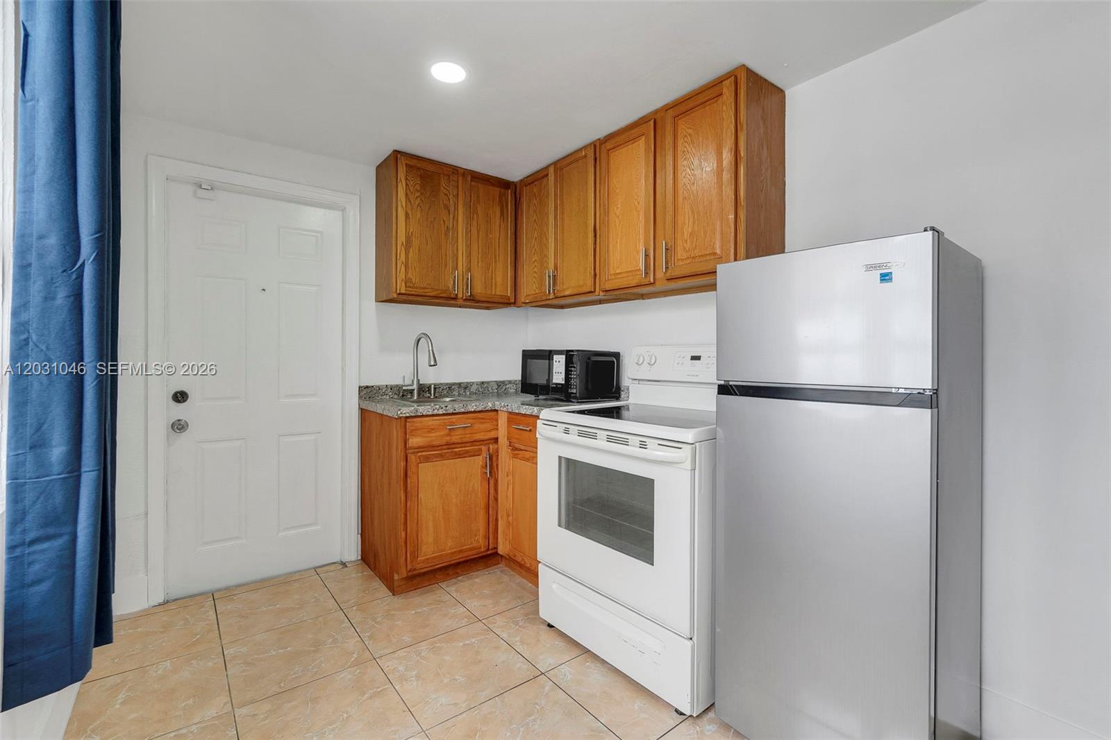 A small kitchen features wooden cabinets, a white stove, a stainless refrigerator, and tile flooring — 6101 SW 24th St # 2, Miramar FL 33023, MIRAMAR, FL