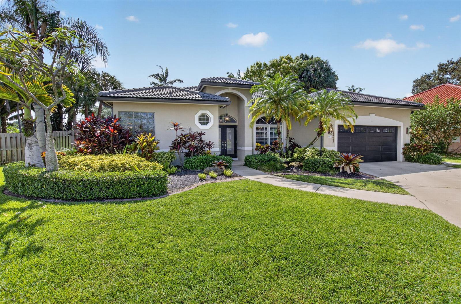 A single-story house with a gray tile roof, dark garage door, and lush tropical landscaping — 1365 E Barwick Ranch Circle, Delray Beach FL 33445, DELRAY BEACH, FL