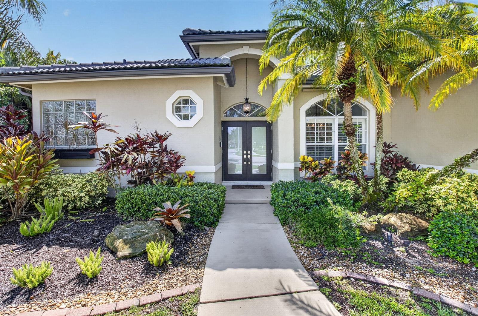 The exterior of a single-story house features a concrete walkway leading to a double-door entrance — 1365 E Barwick Ranch Circle, Delray Beach FL 33445, DELRAY BEACH, FL