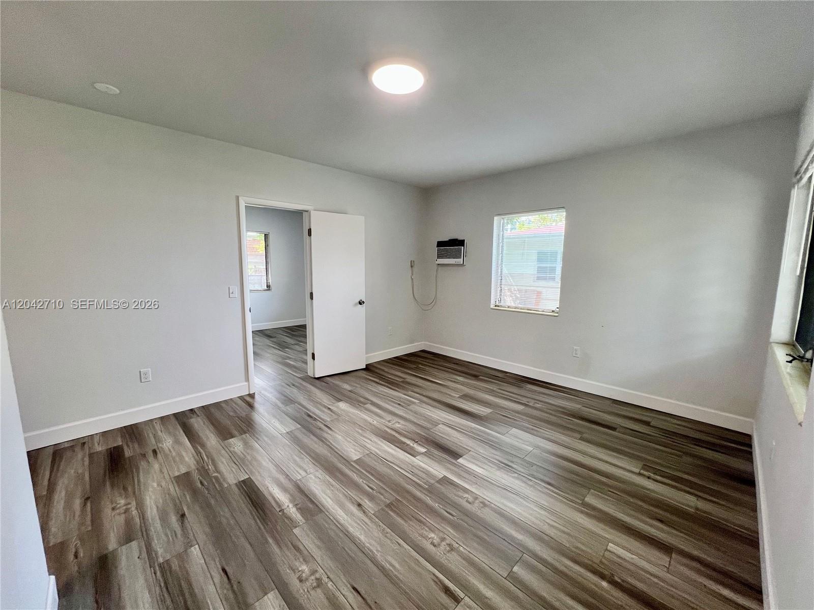 An empty room features light gray walls, wood-look flooring, a window, and an open doorway — 962 NW 6th St # 1, Miami FL 33136, MIAMI, FL