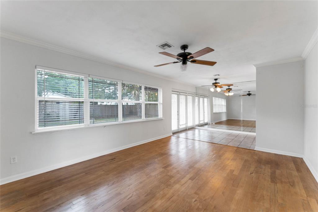 A living room with hardwood floors, a ceiling fan, large windows, and a mirrored wall — 2366 COLDSTREAM DRIVE, WINTER PARK, FL