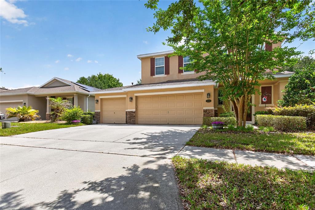 A two-story tan house with a three-car garage and a large tree in the yard — 213 VICTORIA TRAILS BOULEVARD, DELAND, FL
