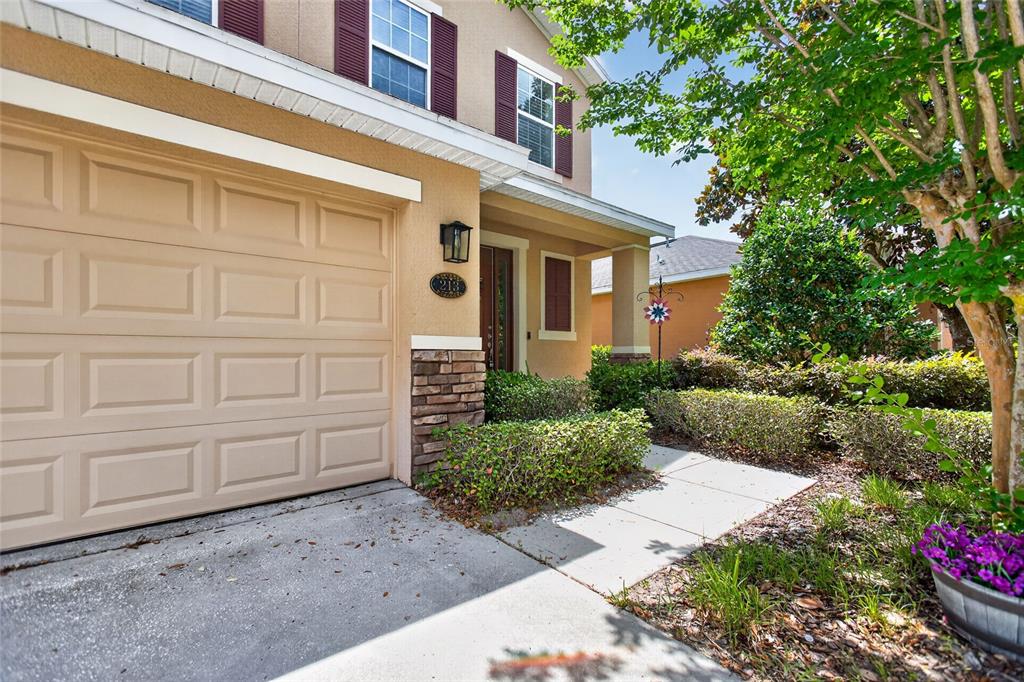 A beige two-story house features a garage, a stone-accented entryway, and landscaped front bushes — 213 VICTORIA TRAILS BOULEVARD, DELAND, FL