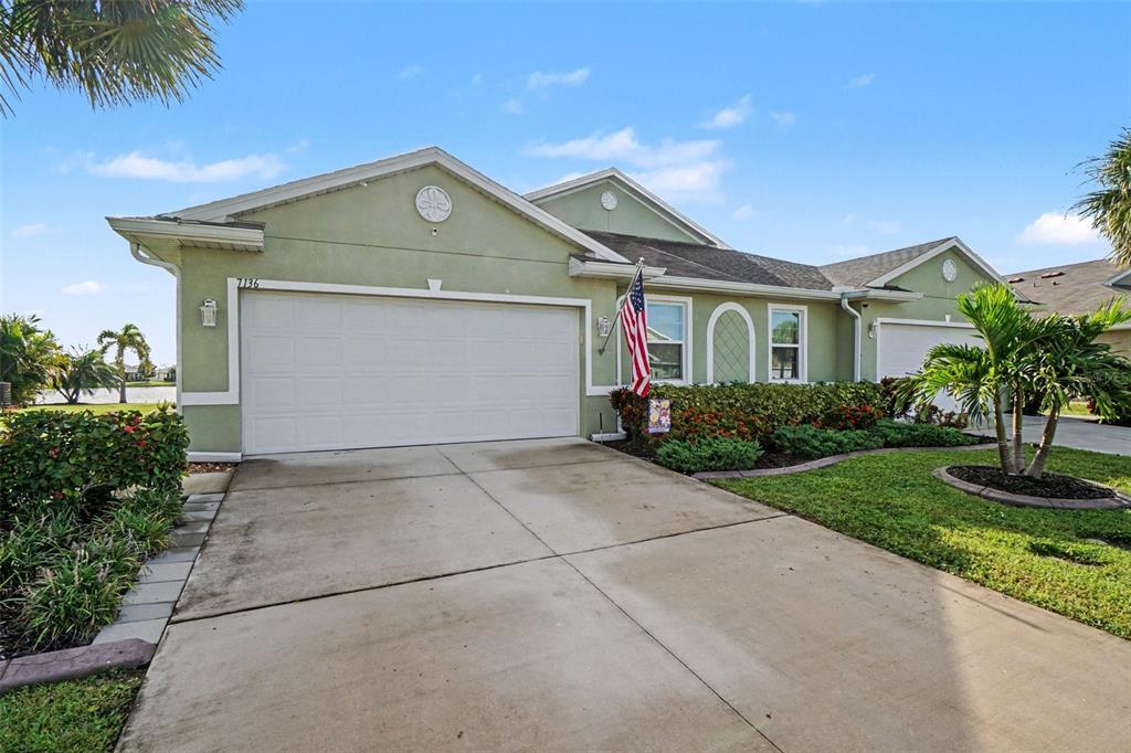 A light green house with a two-car garage, a concrete driveway, and palm trees — 7136 CRYSTAL WAY, PUNTA GORDA, FL