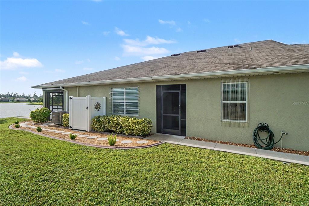 The exterior of a light green house features a screen door, windows, and a landscaped yard — 7136 CRYSTAL WAY, PUNTA GORDA, FL