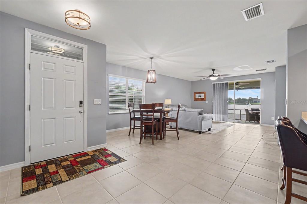 An open-concept living and dining area features light gray walls, tile flooring, and sliding doors — 7136 CRYSTAL WAY, PUNTA GORDA, FL