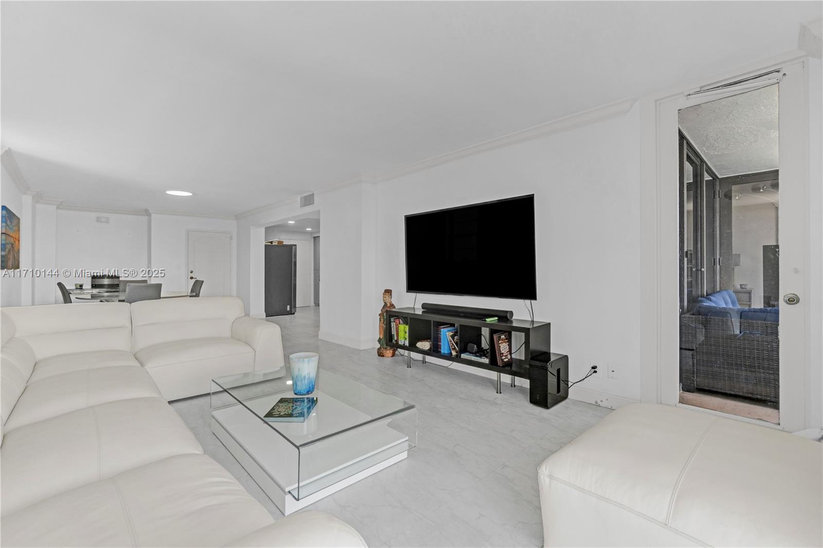 A white living room features a large sectional sofa, glass coffee table, and wall-mounted television — 1600 S Ocean Dr # 2F, Hollywood FL 33019, HOLLYWOOD, FL