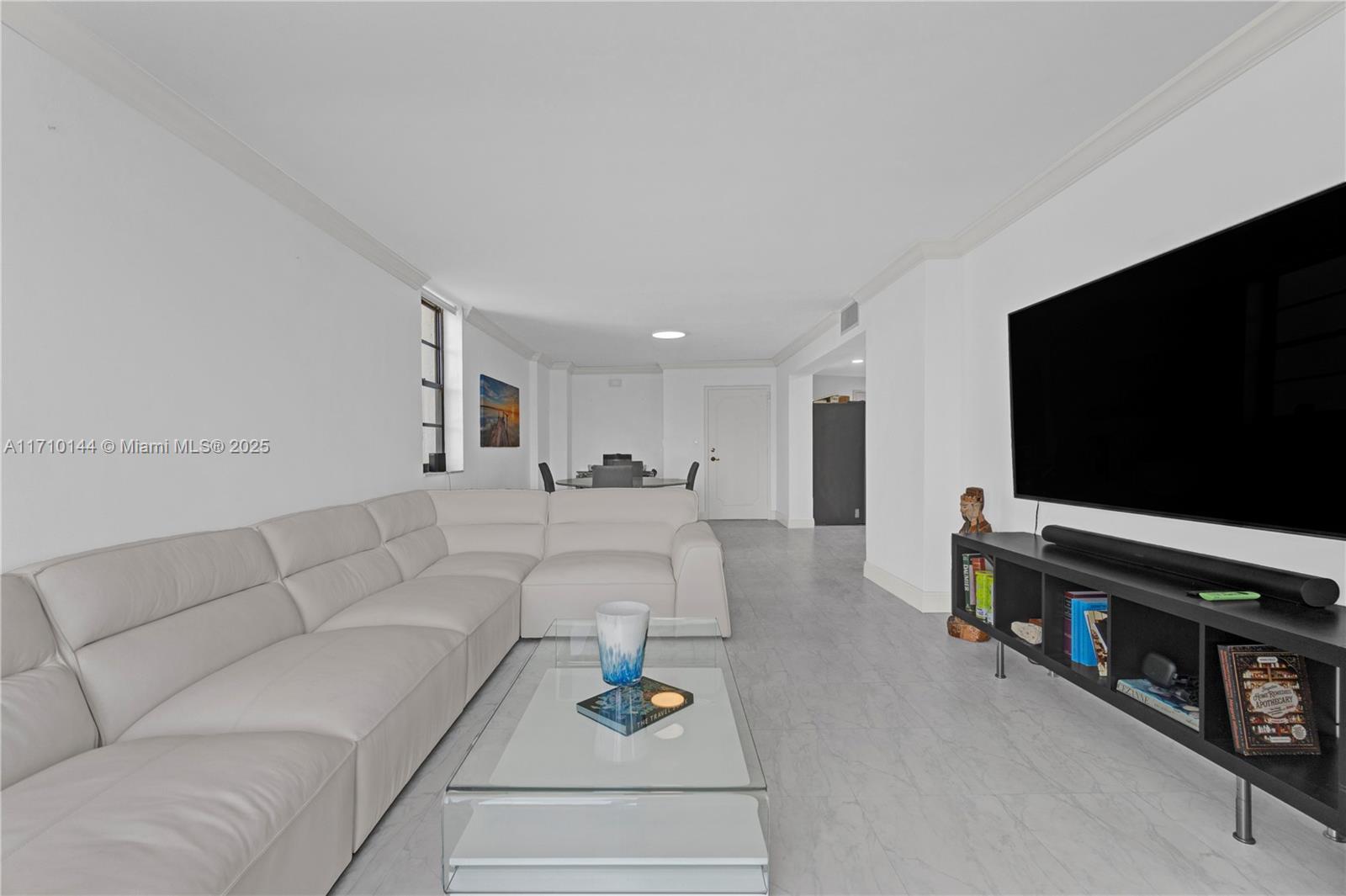 A living room features a white sectional sofa, glass coffee table, and a wall-mounted television — 1600 S Ocean Dr # 2F, Hollywood FL 33019, HOLLYWOOD, FL