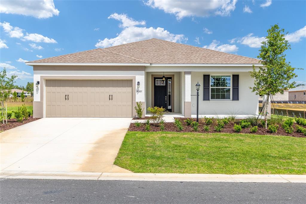 A single-story house with a tan garage, white stucco exterior, and a front porch — 10321 SW 107TH COURT, OCALA, FL