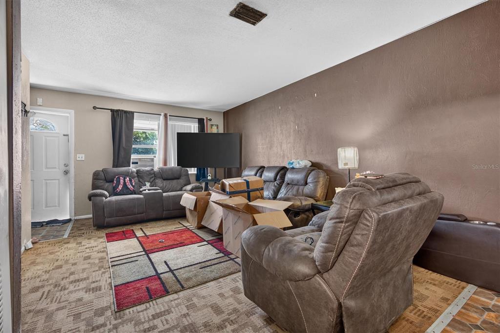 A living room features brown walls, gray reclining furniture, a patterned rug, and cardboard boxes — 1602 S PATRICK CIRCLE, DAYTONA BEACH, FL