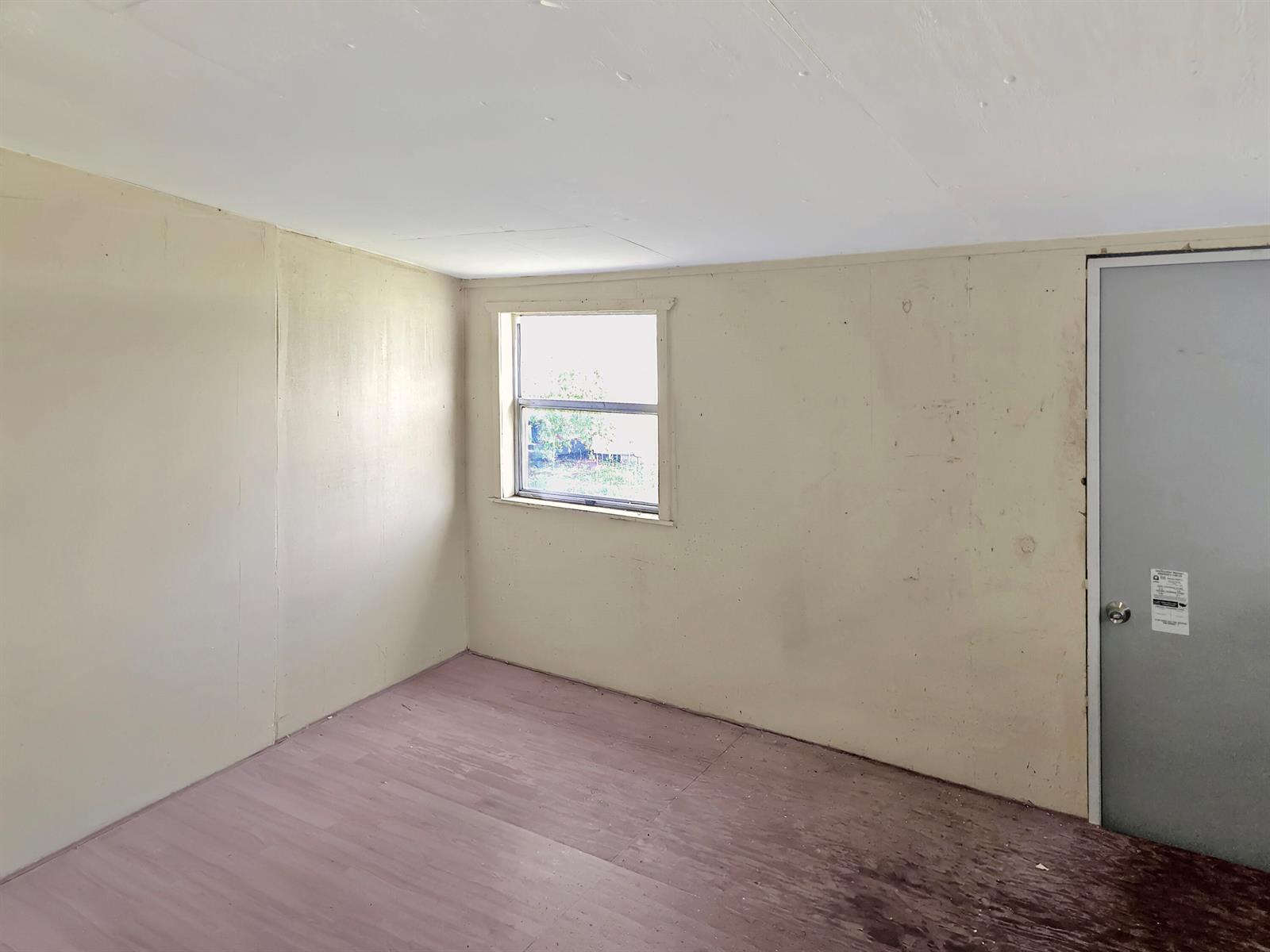 An empty room features beige paneled walls, a single window, and worn wood-look flooring — 314 Dickson Drive, Fort Pierce FL 34982, FORT PIERCE, FL
