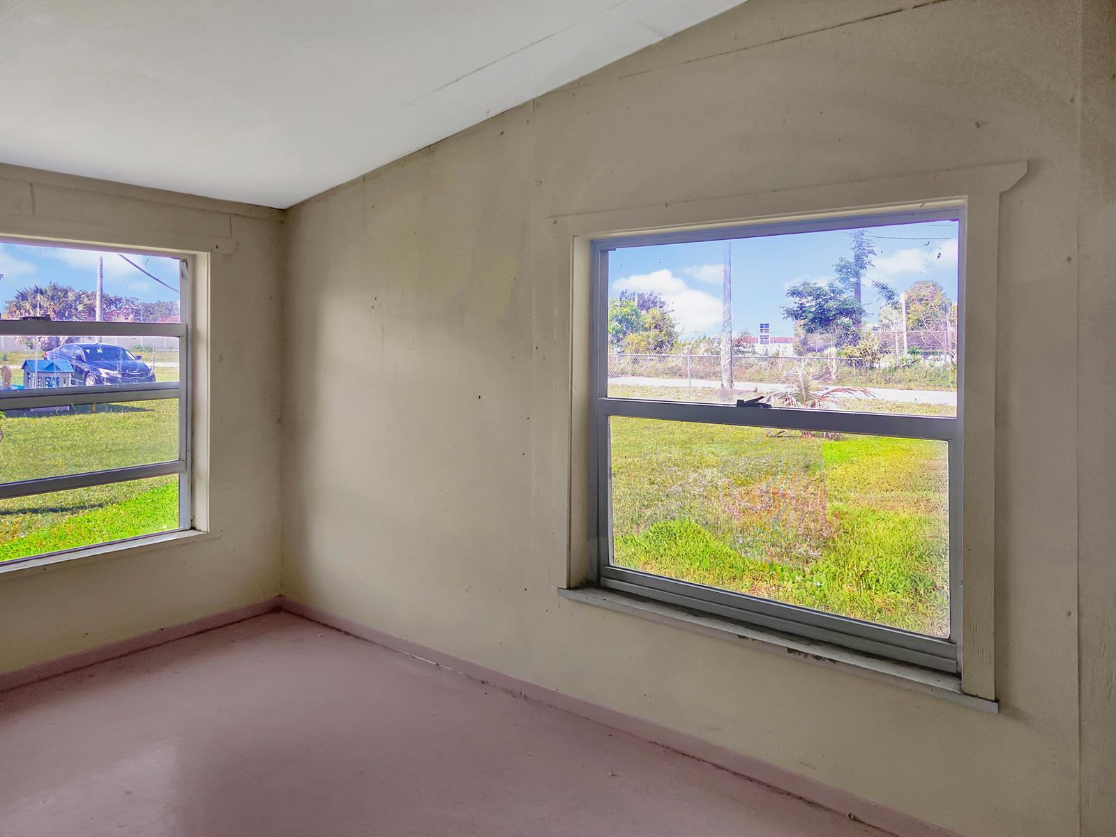An empty room with light-colored walls, pink flooring, and two windows overlooking a grassy yard — 314 Dickson Drive, Fort Pierce FL 34982, FORT PIERCE, FL