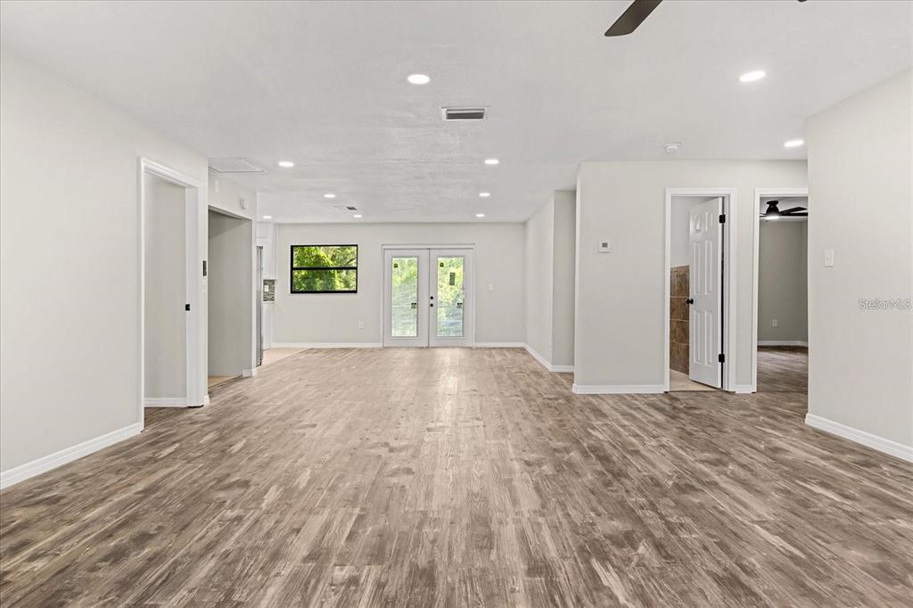 A spacious, empty room features light gray walls, wood-look flooring, recessed lighting, and French doors — 575 LAKE MCCOY DRIVE, APOPKA, FL