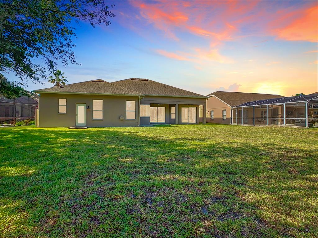 The rear exterior of a tan house features a large lawn and a screened-in patio — 4925 BRIGHTMOUR CIRCLE, ORLANDO, FL