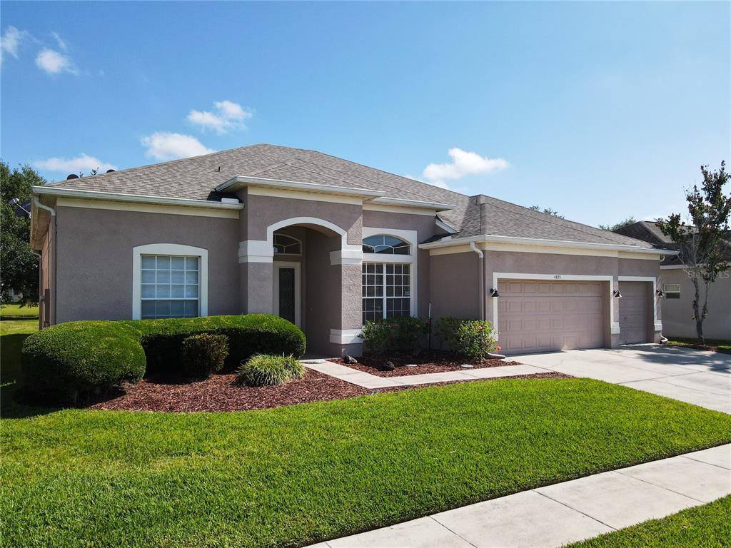 A single-story stucco house features a multi-car garage, a front entryway, and a landscaped lawn — 4925 BRIGHTMOUR CIRCLE, ORLANDO, FL