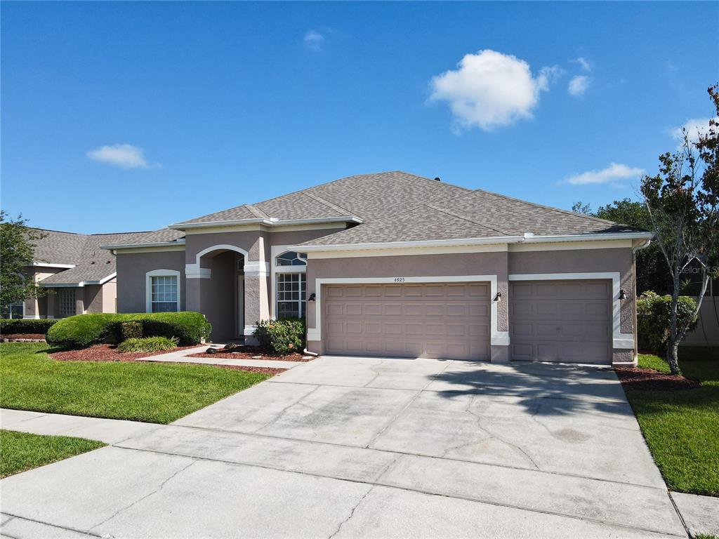 A single-story suburban house with a tan stucco exterior and a three-car garage — 4925 BRIGHTMOUR CIRCLE, ORLANDO, FL