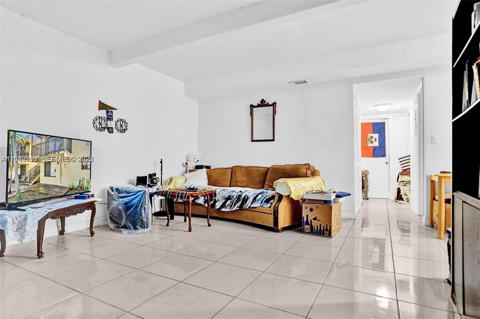 A living room features white walls, light-colored tile floors, a brown sofa, and a television — 1065 S Flagler Ave # 704, Pompano Beach FL 33060, POMPANO BEACH, FL
