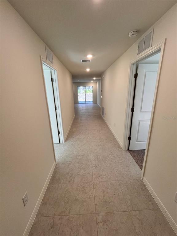 A long hallway with light-colored tile flooring leads toward a glass sliding door — 10450 BAYLOR AVENUE, HASTINGS, FL