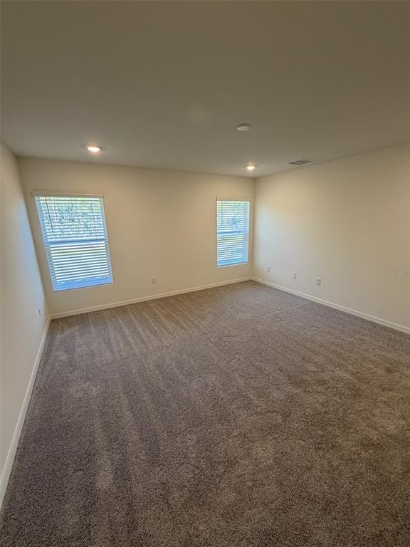 An empty bedroom with beige walls, carpeted flooring, and two windows with white blinds — 10450 BAYLOR AVENUE, HASTINGS, FL