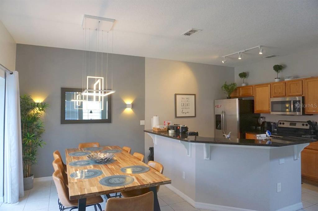 A dining area with a wooden table and pendant light adjacent to an open kitchen — 3162 YELLOW LANTANA LANE, KISSIMMEE, FL