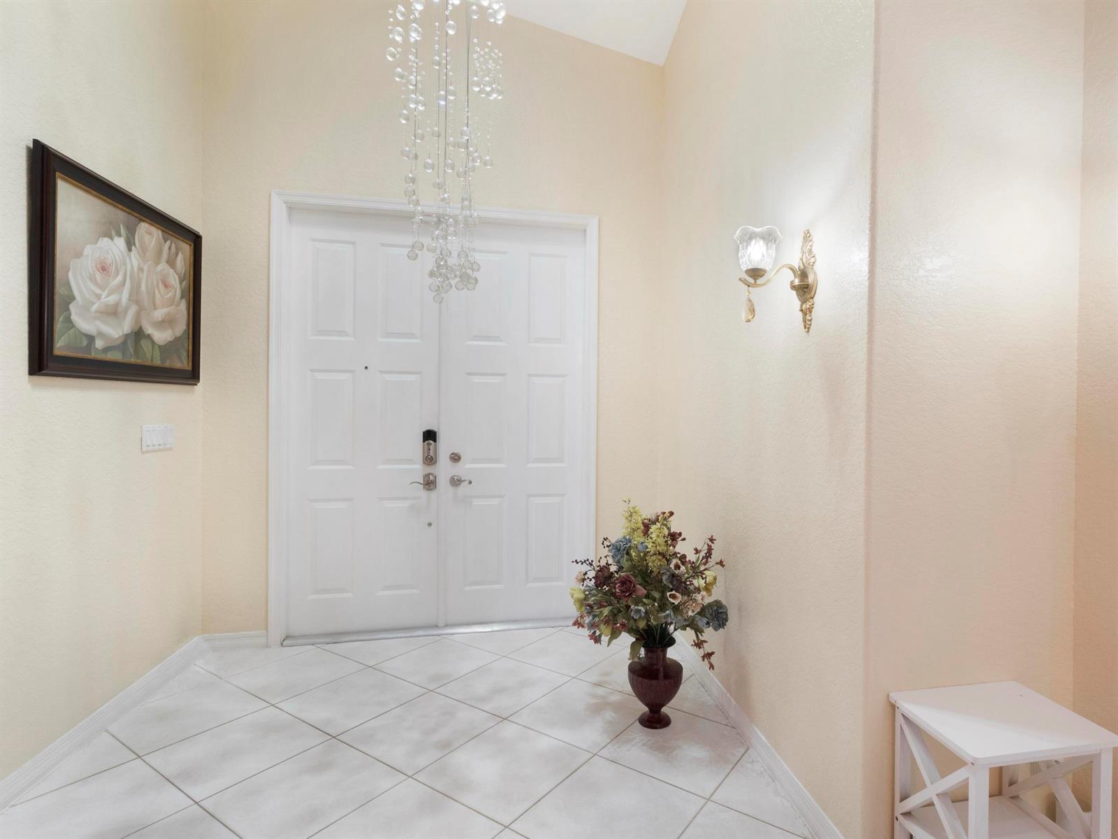 A bright entryway features white double doors, a crystal chandelier, and light-colored tile flooring — 5159 Brookview Drive, Boynton Beach FL 33437, BOYNTON BEACH, FL