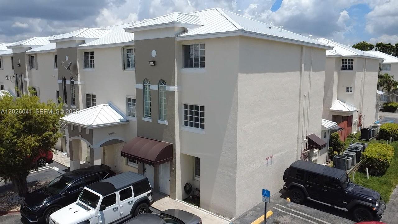An exterior view of a multi-story residential building with beige stucco walls and parked vehicles — 12015 SW 14 st # 301-C, Miami FL 33184, MIAMI, FL