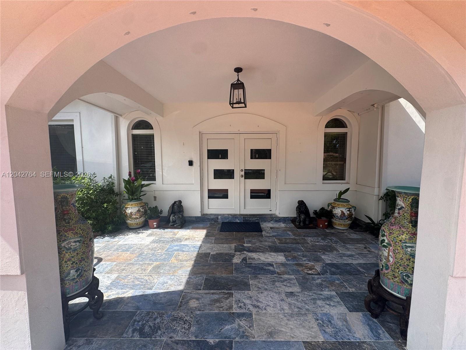 A covered entryway features stone tile flooring, double doors, and two large decorative ceramic vases — 7935 SW 128th St, Pinecrest FL 33156, PINECREST, FL