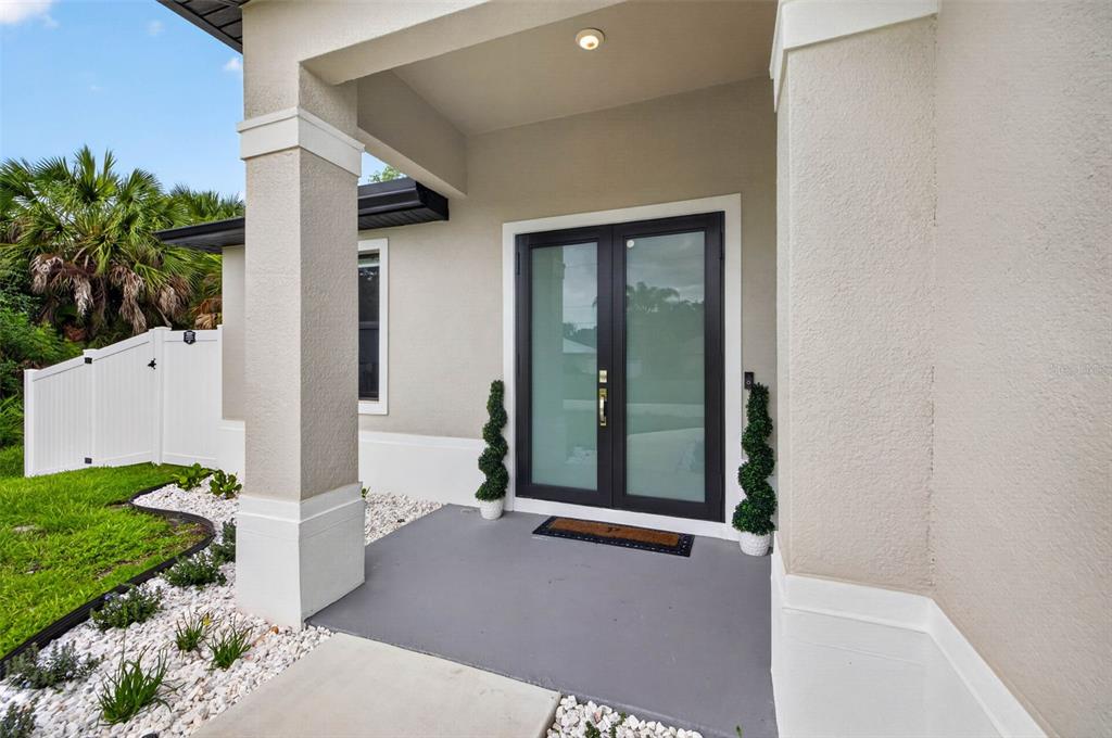 A covered entryway features a gray concrete porch, double glass doors, and two potted topiaries — 3772 PARKINS TERRACE, NORTH PORT, FL