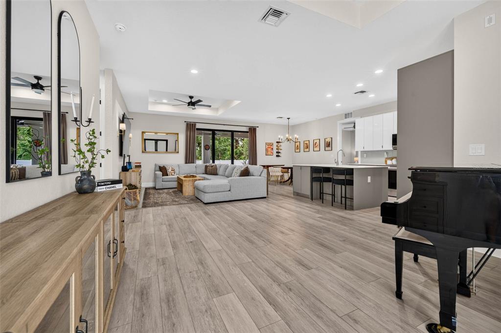 A spacious open-concept living area features light wood-look flooring, a kitchen island, and a piano — 3772 PARKINS TERRACE, NORTH PORT, FL