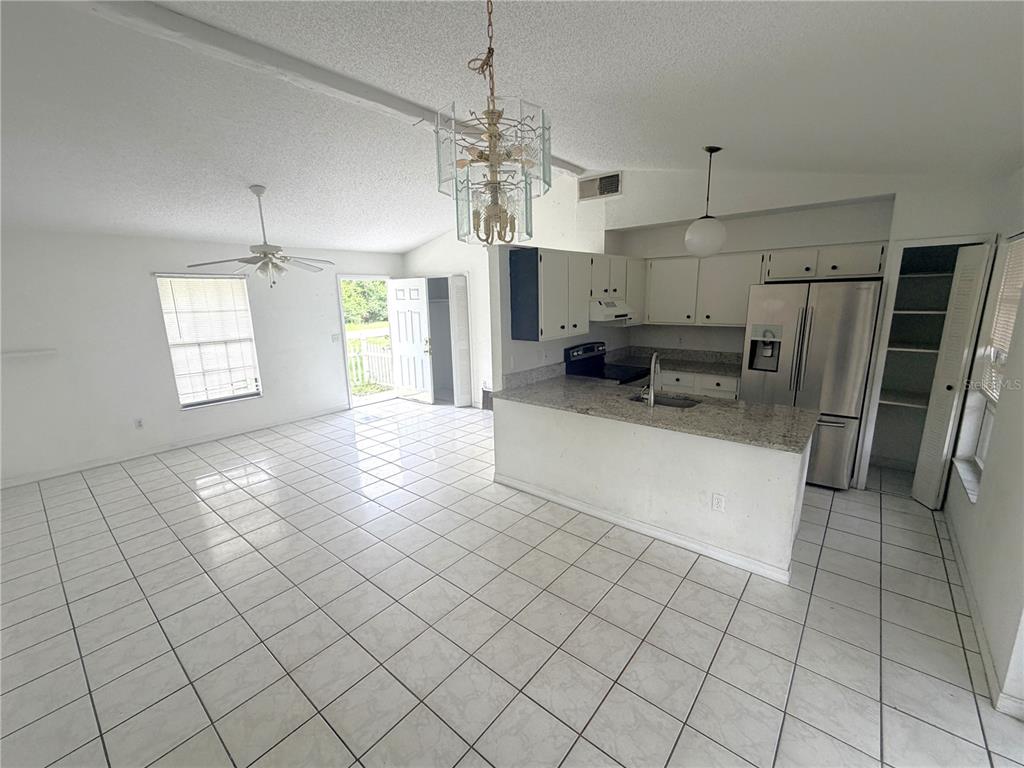 An open-concept kitchen and living area features white tile flooring, white cabinetry, and granite countertops — 745 WHITEWOOD DRIVE, DELTONA, FL