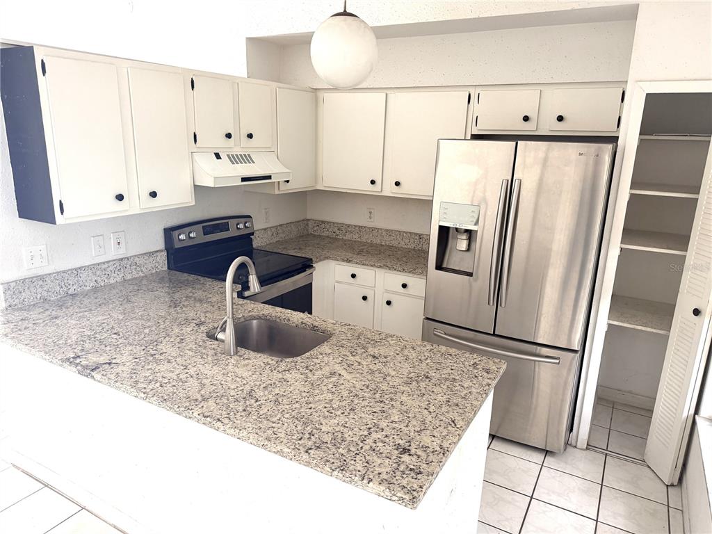 A kitchen features white cabinets, granite countertops, stainless steel appliances, and a tile floor — 745 WHITEWOOD DRIVE, DELTONA, FL