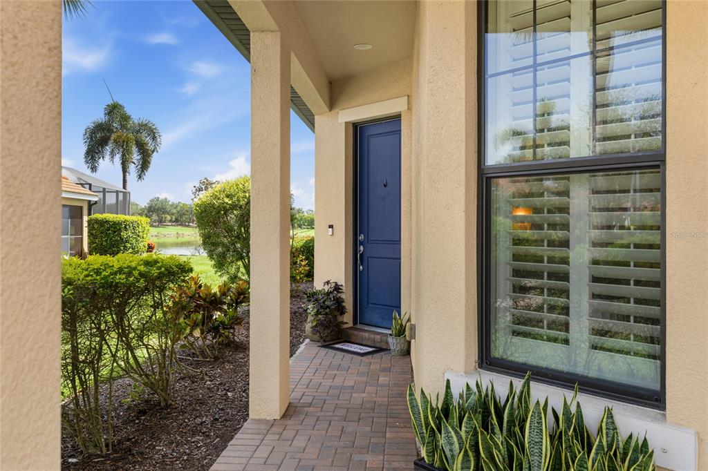 A blue front door is set back under a covered porch with brick pavers — 10496 CROOKED CREEK DRIVE, VENICE, FL