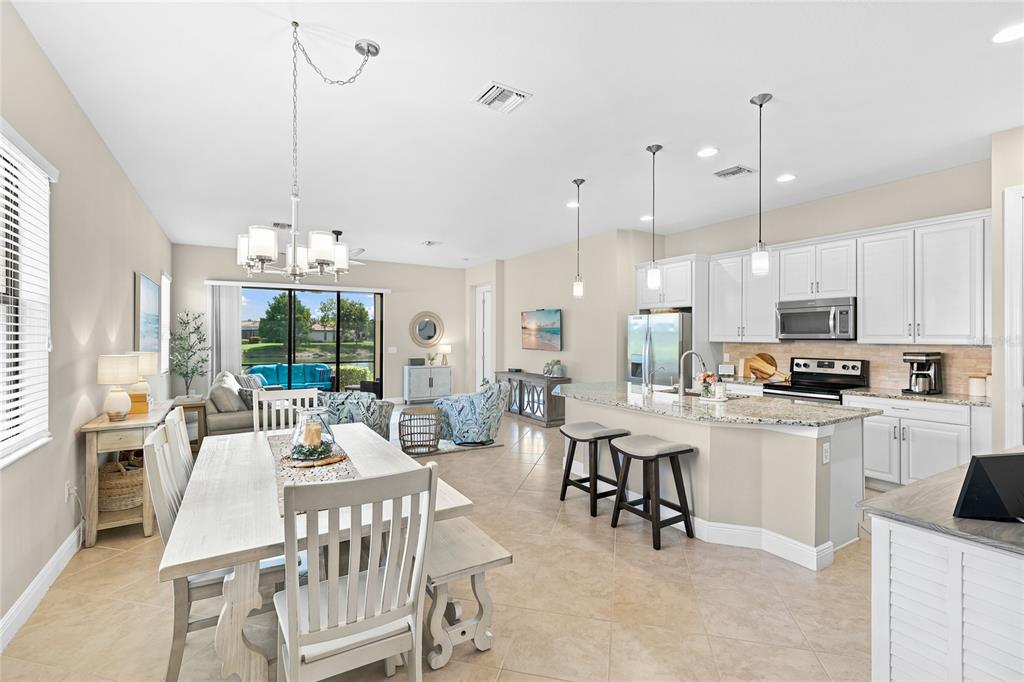 An open-concept kitchen and dining area features white cabinets, granite countertops, and tile flooring — 10496 CROOKED CREEK DRIVE, VENICE, FL