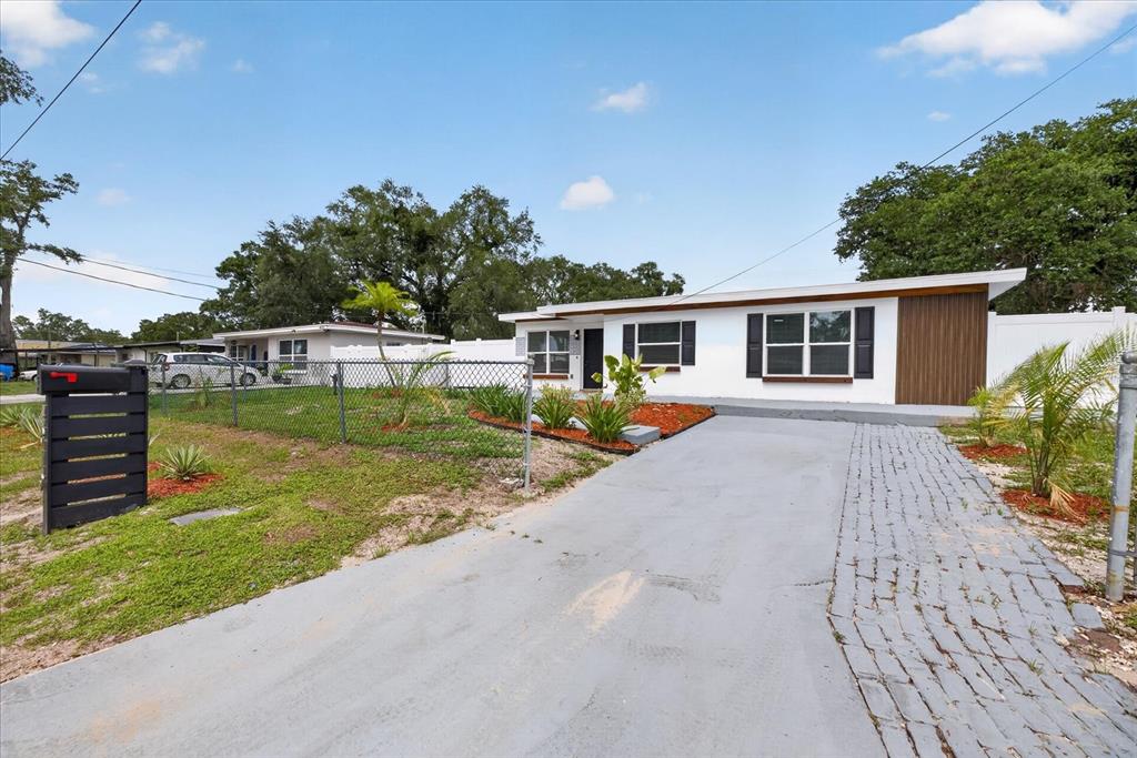 A white single-story house features a gray driveway, a chain-link fence, and a wood-paneled accent — 4019 MCLANE DRIVE, TAMPA, FL