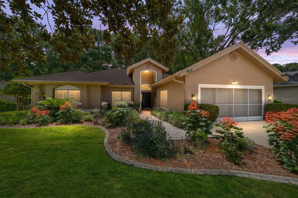 A single-story house with a tan stucco exterior, a paved walkway, and landscaped front gardens — 11465 SW 82ND COURT ROAD, OCALA, FL