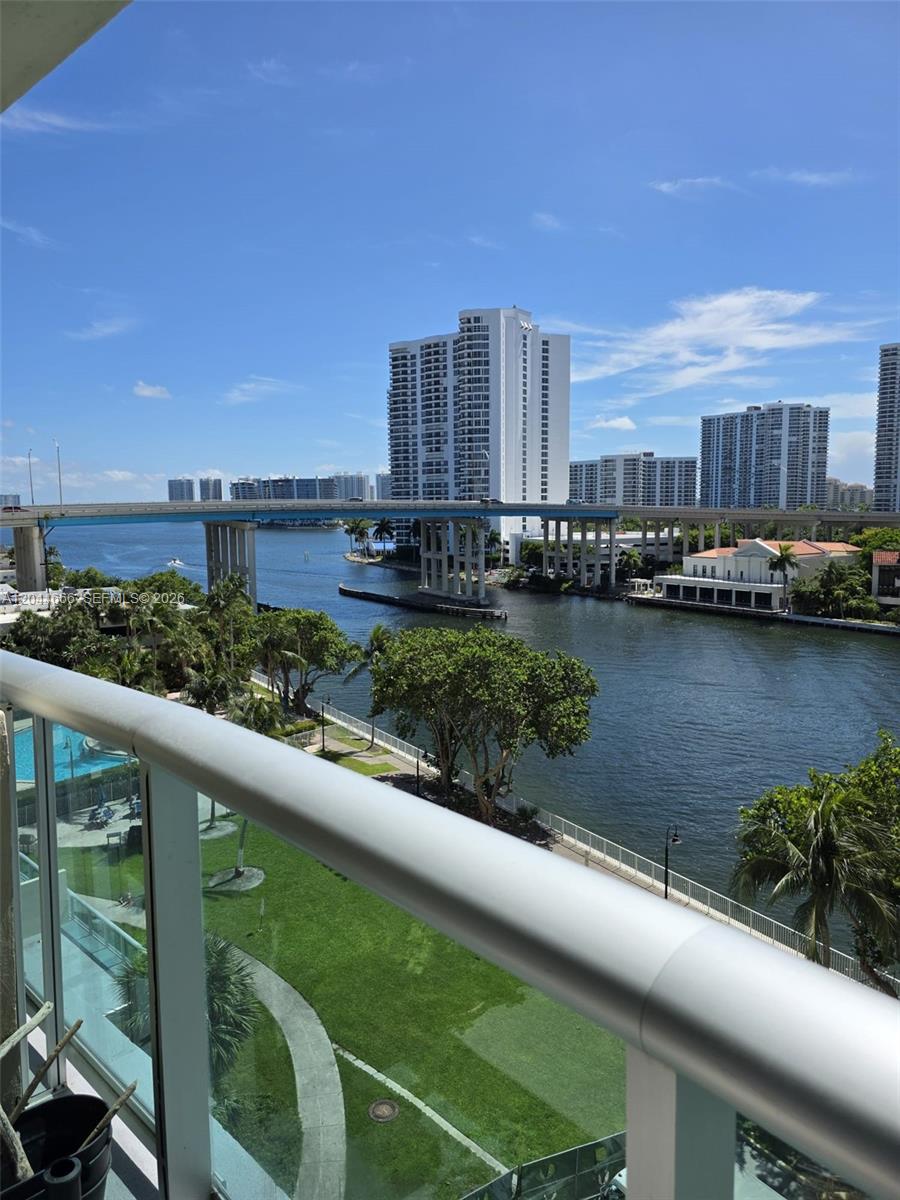 A balcony view overlooks a waterway, a bridge, and high-rise buildings under a blue sky — SUNNY ISLES BEACH, FL