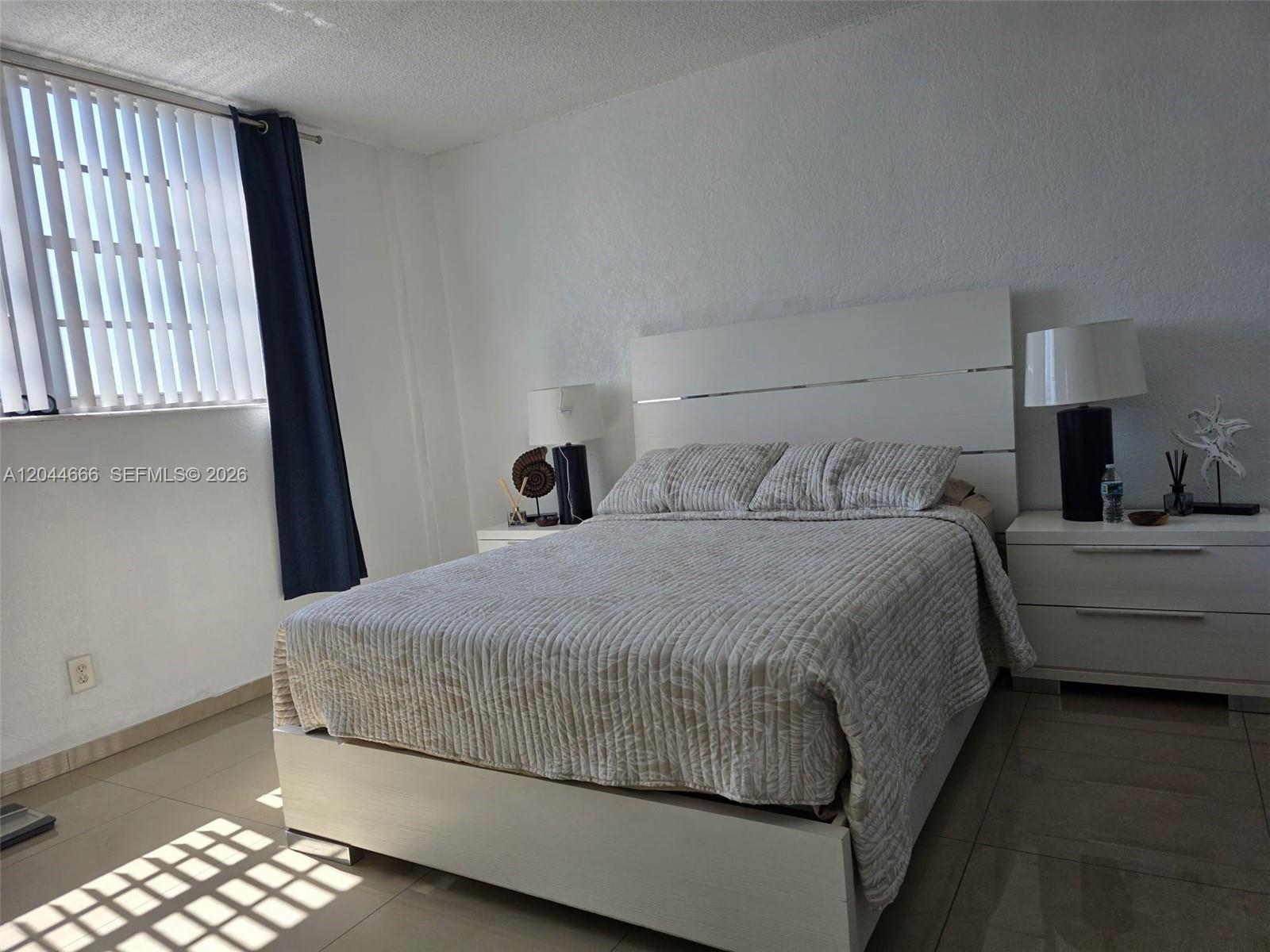 A bedroom features a white bed frame, a patterned quilt, and two matching nightstands — SUNNY ISLES BEACH, FL