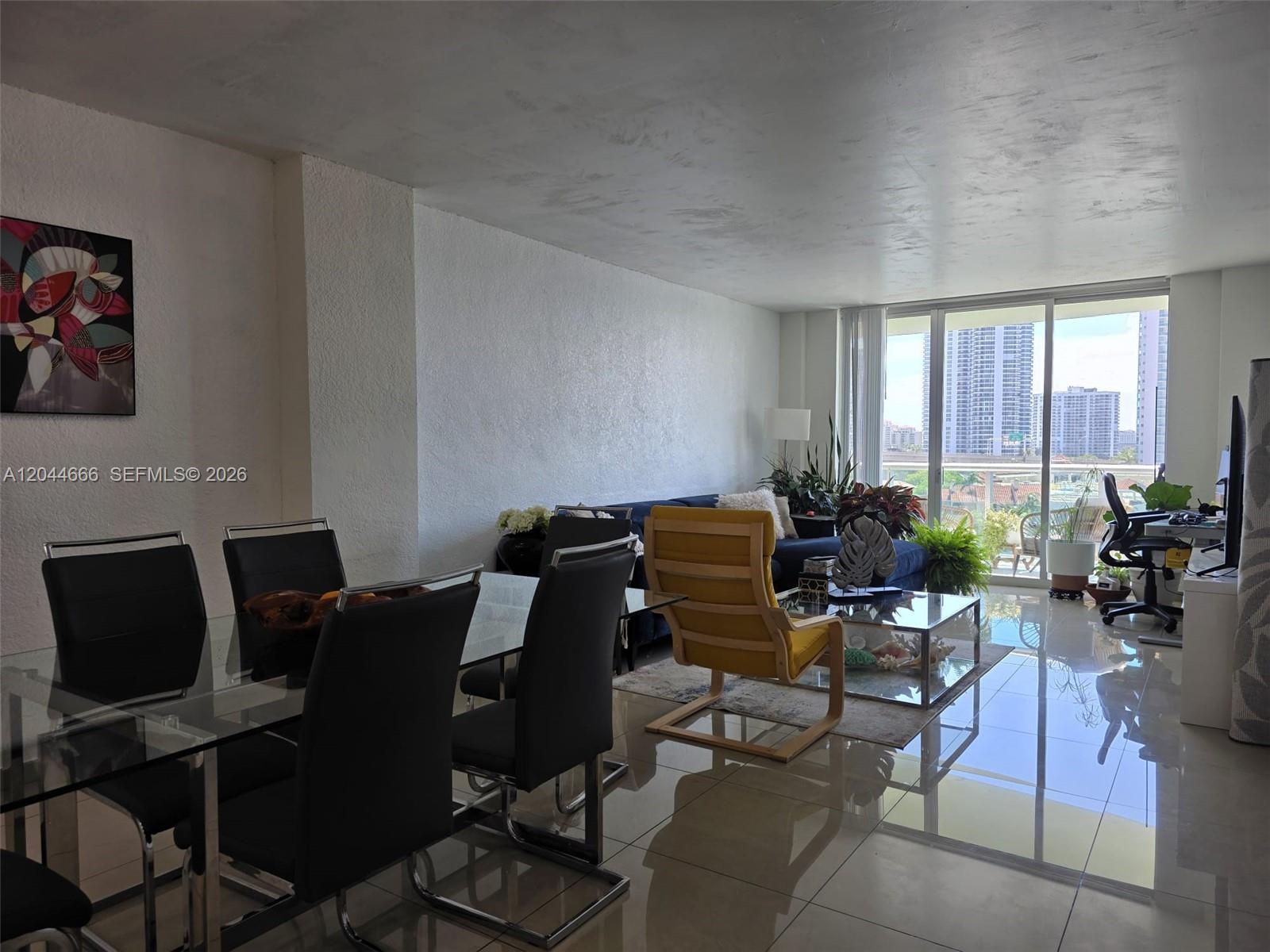 A bright living and dining area features tile floors, a glass table, and balcony views — SUNNY ISLES BEACH, FL
