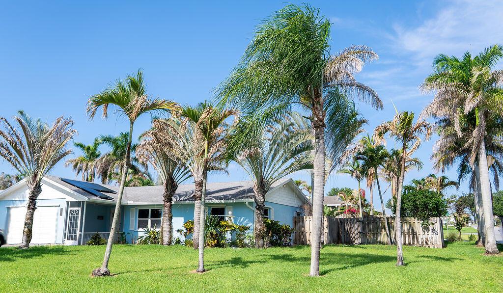 A light blue single-story house with a white garage and several tall palm trees — 2445 NE 16th Court, Jensen Beach FL 34957, JENSEN BEACH, FL