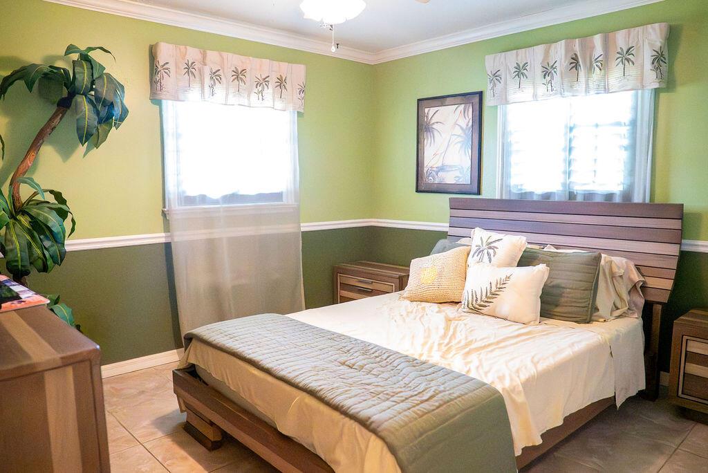 A bedroom features green walls, a wooden bed frame, tile flooring, and two windows — 2445 NE 16th Court, Jensen Beach FL 34957, JENSEN BEACH, FL