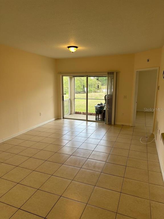 A living room with beige tile flooring, a ceiling light, and sliding glass doors to a patio — 6425 CYPRESSDALE DRIVE UNIT 101, RIVERVIEW, FL