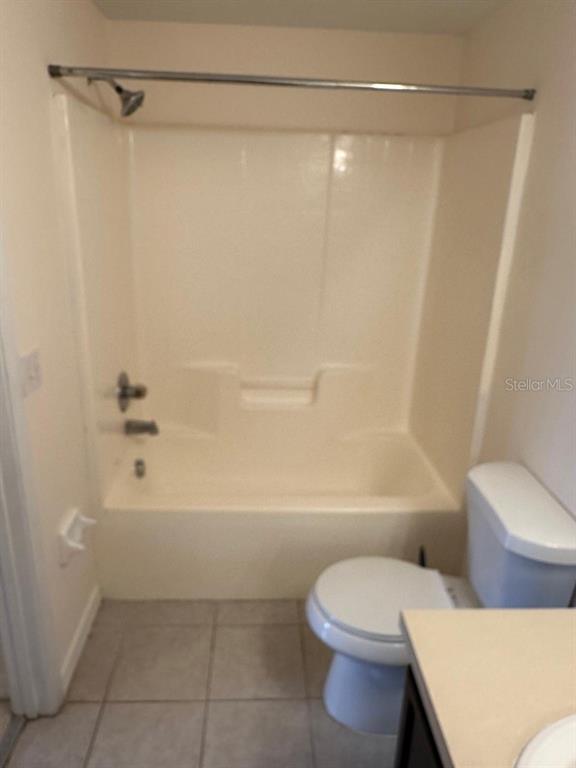 A bathroom featuring a beige bathtub-shower combination, a white toilet, and tiled flooring — 6425 CYPRESSDALE DRIVE UNIT 101, RIVERVIEW, FL