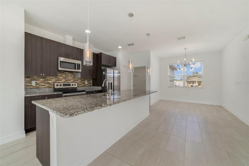 A modern kitchen features dark wood cabinets, granite countertops, and a large island with pendants — 212 GROUPER COURT, POINCIANA, FL