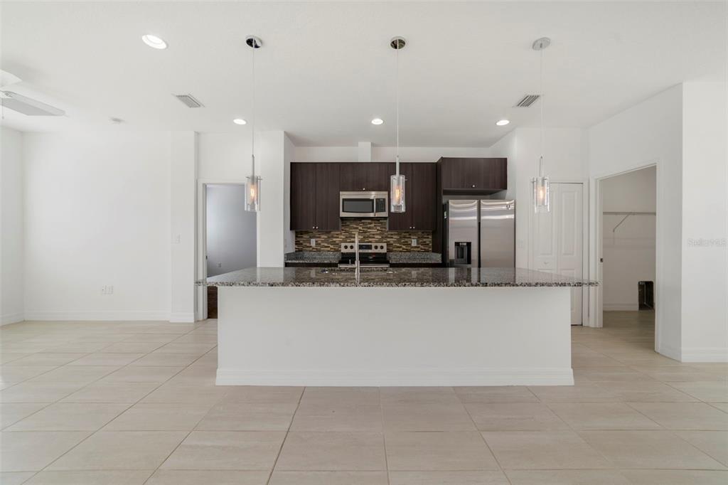 A modern kitchen features dark wood cabinets, granite countertops, a large island, and pendant lighting — 212 GROUPER COURT, POINCIANA, FL