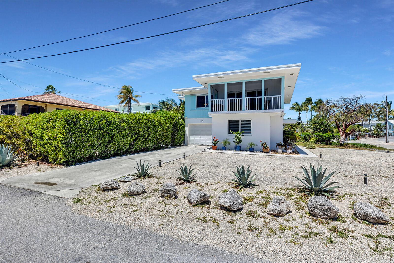 A two-story house with a screened balcony, white garage, and gravel yard with desert landscaping — 309 Jasmine Street, FL 33050, FL