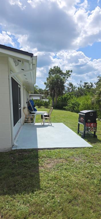 A concrete patio sits outside a house with a small table, two chairs, and a grill — 460 CREEK LANE DRIVE, ENGLEWOOD, FL
