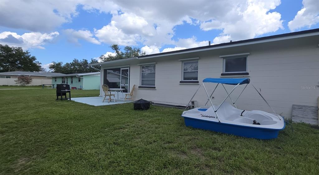 A backyard view shows a white house with a patio, a grill, and a pedal boat — 460 CREEK LANE DRIVE, ENGLEWOOD, FL